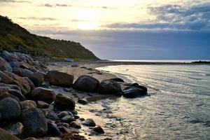 Sunset on the Danish coast. Beach, waves. Hill with trees in background. Landscape photo