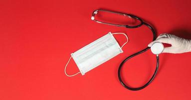 Hand with glove is holding STETHOSCOPE.It have mask put on red background. photo