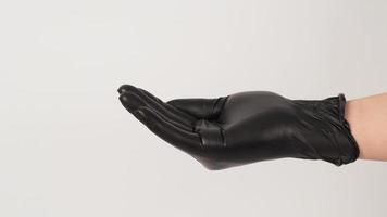 la mano lleva un guante de látex negro y suplica el signo de la mano en el fondo blanco. foto