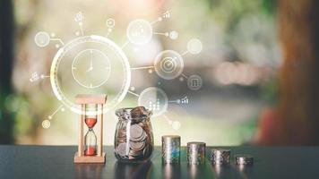 The hourglass, the coin, and the glass jar, all on the table,time management concepts for saving money,Finance and Investment, Profit Growth and Dividends,Effective goal setting and management photo