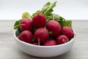 Red radishes in a white bowl isolated on wooden background photo