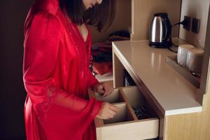 una mujer con un camisón rojo abre un cajón y encuentra algo en la cocina. no se puede encontrar, artículos perdidos foto
