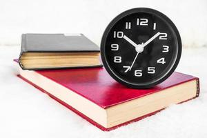 Black alarm clock and book stacked on table photo