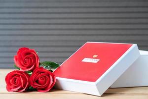 Red roses and heart-shaped box on wood background photo