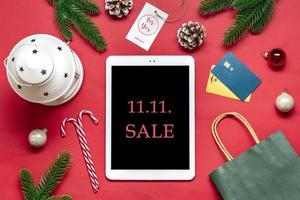 Tablet with black screen, debit card, Xmas decor, bag, boxes on red table Top view Flat lay Holiday shopping list, Happy New Year, Christmas online shop, chooses gifts, makes purchases concept Mock up photo