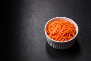 Tasty spicy Korean carrot with spices and herbs on a dark concrete background photo