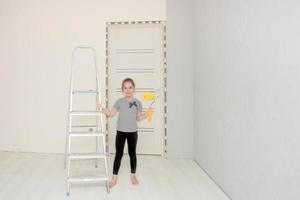 linda chica en la habitación donde se está realizando la renovación se encuentra junto a la escalera y sostiene un rodillo de pintura en la mano foto