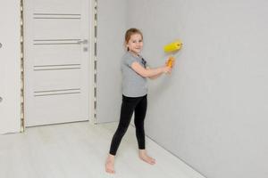 la niña conduce a lo largo de la pared con un rodillo de pintura en una casa que se está renovando. foto