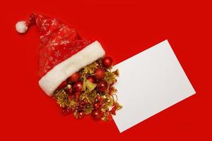 Christmas toys spill out of santa's hat, next to an empty white sheet on a red background, copyspace, christmas content photo