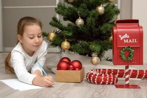 Girl by the Christmas tree writes a letter to Santa, Christmas content photo