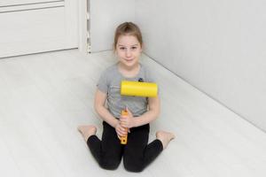 cute girl is sitting on the floor in the room where the renovation is going on, holding a paint roller in her hands and smiling photo