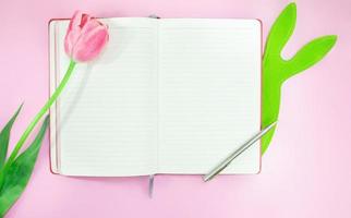 Tulip and green felt hare with notebook and pen on pink background. Easter. Copy space photo