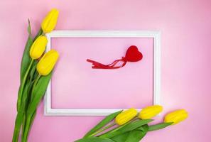 Yellow tulips with frame and red heart with place for text on pink background. Holiday, Birthday, 8 March, Mother's, International Women's Day. Copy space photo