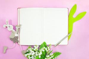 Notepad for text with pen. Bouquet of lilies of valley and rabbits on pink background. Easter. Copy space photo