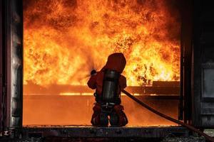 Firefighter Rescue training to stop burning flame, Fireman wear hard hat and safety uniform suit for protection burn using hose with chemical water foam spray. photo