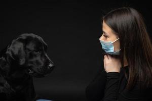 Portrait of a Labrador Retriever dog in a protective medical mask with a female owner. photo
