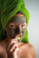 Beautiful young woman with facial mask on her face holding slices of cucumber. photo