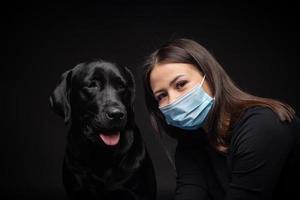 Portrait of a Labrador Retriever dog in a protective medical mask with a female owner. photo