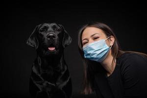 Portrait of a Labrador Retriever dog in a protective medical mask with a female owner. photo