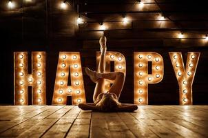 una chica en traje de baño y zapatillas de deporte está sentada en el suelo. la palabra felicidad se destaca en letras grandes y brillantes foto