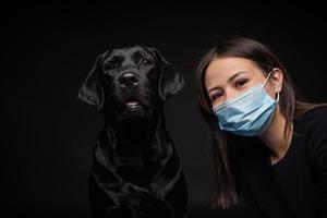 Portrait of a Labrador Retriever dog in a protective medical mask with a female owner. photo