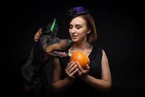 Portrait of a Doberman dog with a girl owner. In carnival costumes with a pumpkin. photo