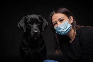 Portrait of a Labrador Retriever dog in a protective medical mask with a female owner. photo