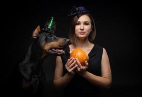 Portrait of a Doberman dog with a girl owner. In carnival costumes with a pumpkin. photo