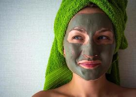 Young woman with clay mask on her face against light background, space for text. photo
