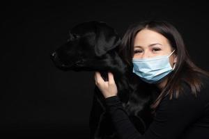 Portrait of a Labrador Retriever dog in a protective medical mask with a female owner. photo