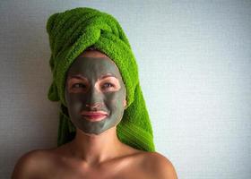 Young woman with clay mask on her face against light background, space for text. photo