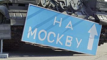 señal de carretera azul con letras blancas cerca del tanque, en el territorio del museo nacional de historia de ucrania. la guerra de rusia contra ucrania. traducción, a moscú. video