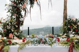hermosa configuración de altar blanco de boda al aire libre con tema rústico, jarrones de ceremonia de arena de boda con vidrio alineado con decoración de flores naturales y fondo de montaña.