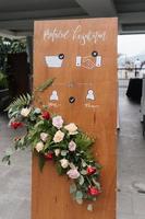 A front board sign translate in Indonesia say Health protocol, with flower decoration standing at the wedding entrance. photo