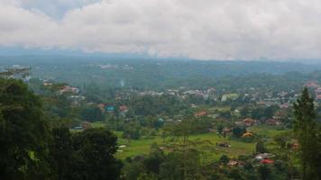 la vista del cielo nublado, árboles, montañas y casas fue fotografiada desde arriba de la colina foto