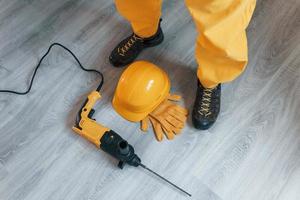 Handyman in yellow uniform with drill standing indoors. House renovation conception photo