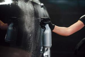 Spraying the vehicle. Modern black automobile get cleaned by woman inside of car wash station photo