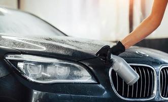 Spraying the vehicle. Modern black automobile get cleaned by woman inside of car wash station photo