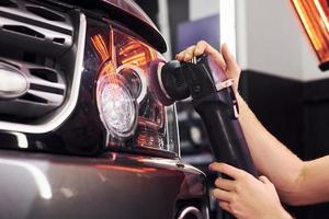 Guy polishing surface of vehicle. Modern black automobile get cleaned by man inside of car wash station photo