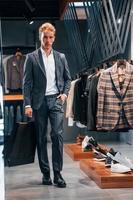 Walks with bag in hand. Young guy in modern store with new clothes. Elegant expensive wear for men photo