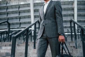 sostiene la bolsa en las manos. un joven hombre de negocios con ropa formal gris está al aire libre en la ciudad foto