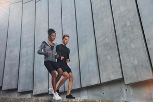 cerca de la gran pared. el hombre europeo y la mujer afroamericana en ropa deportiva hacen ejercicio juntos foto