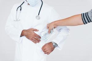 Medic takes bribe. Close up particle view of young man that standing indoors against white background photo