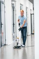 Young man works in the modern office. Uses vacuum cleaner photo