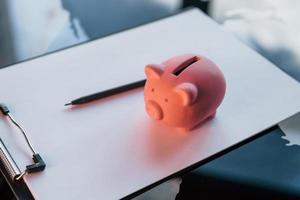 Close up view of pink piggy bank that lying on the white document on table photo