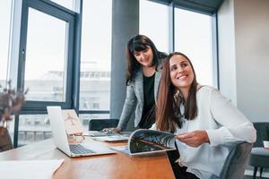 Two women in formal clothes is indoors in the modern office works together photo