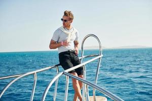 Posing for a camera. Young male tourist is on the yacht on the sea. Conception of vacation photo