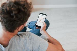 Holds phone. Rear view of adult man that is indoors controlling smart home technology photo