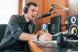 Talks and uses mic. Young man is indoors in the radio studio is busy by broadcast photo