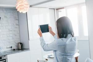 Digital tablet in hands. Young woman is indoors in smart house room at daytime photo